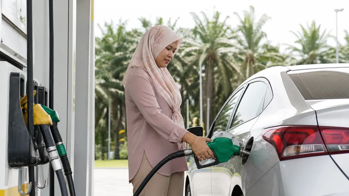 A woman in a hijab fills up a sedan at a petrol station pump in the morning