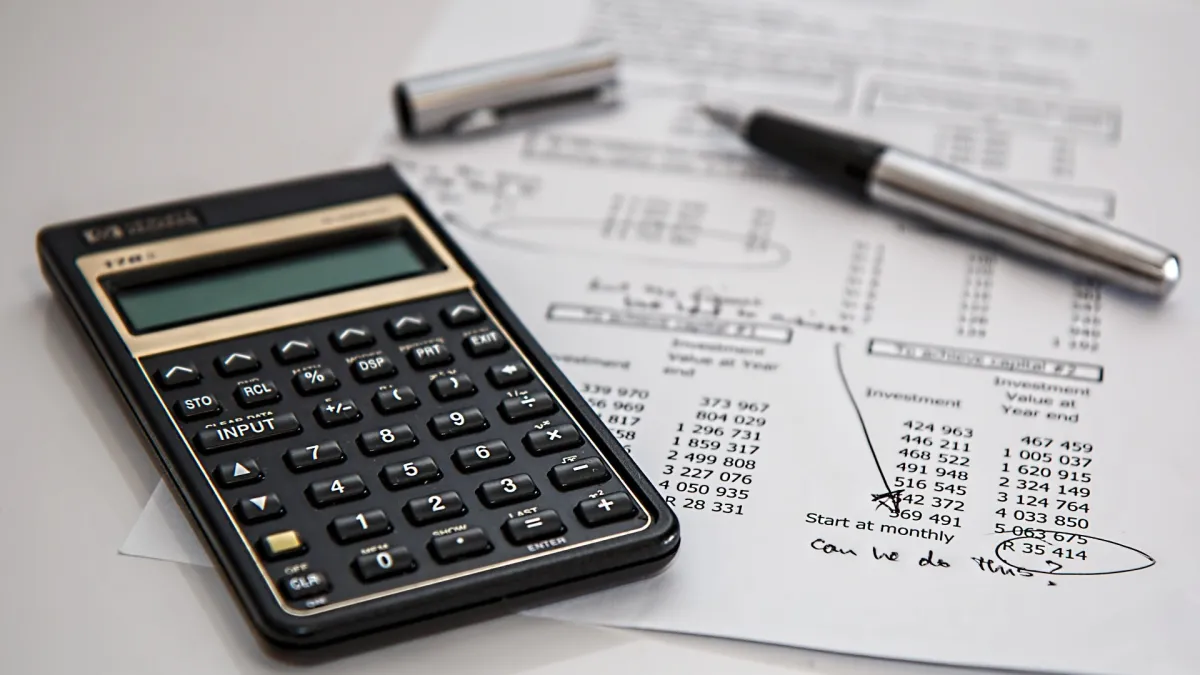 Financial calculator and pen on paper with tables of figures