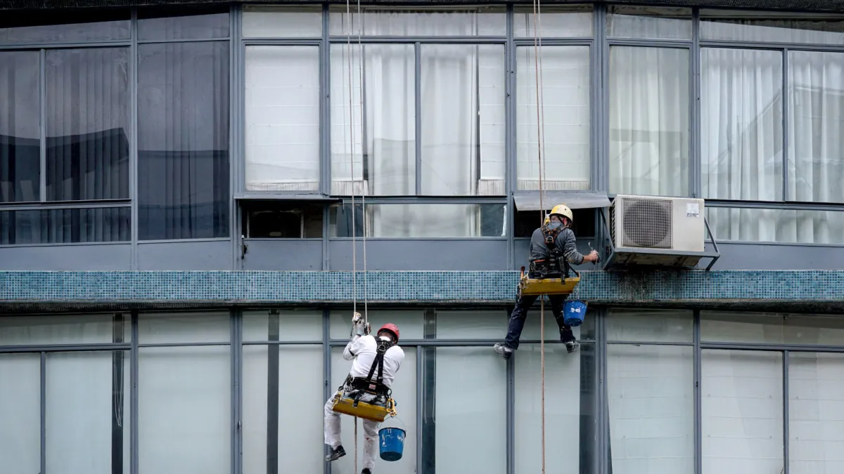 Two workers on ropes cleaning the windows of a building