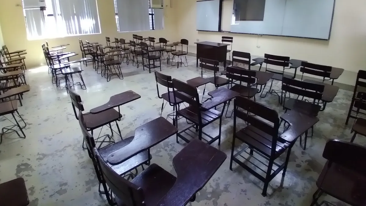 An empty classroom with rows of wooden desk chairs