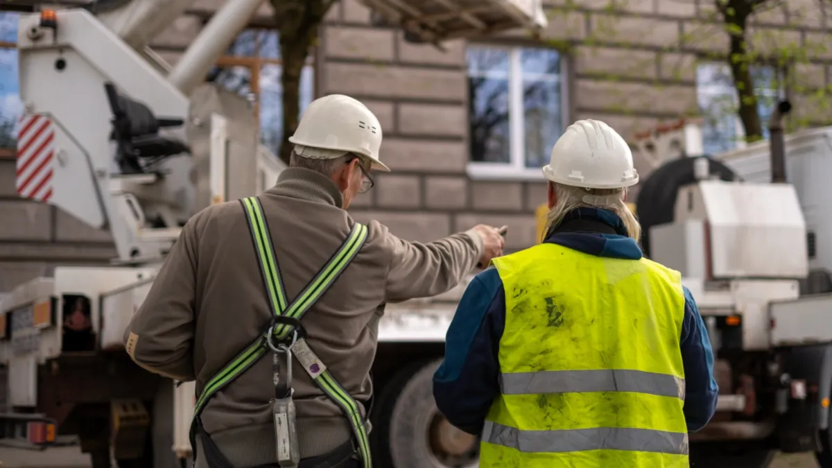 Two workers in safety helmets at a work site, seen from behind