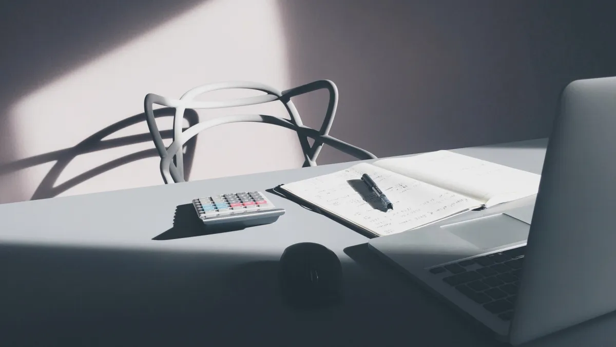 A calculator, a notebook and a laptop on a desk